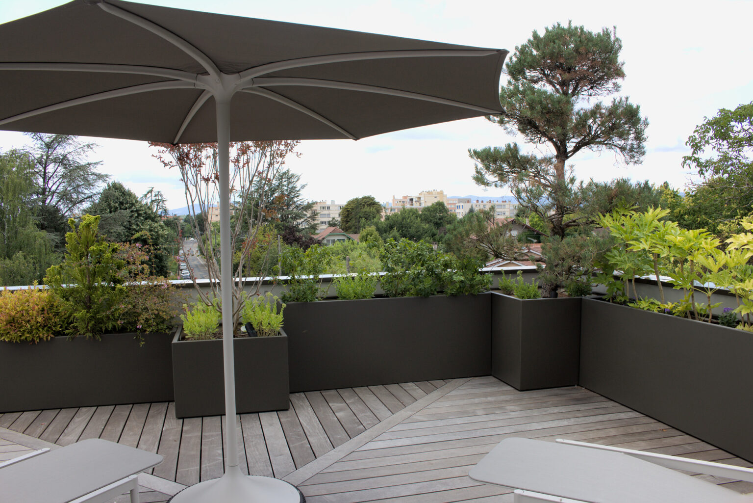 Parasol gris sur terrasse ipé en chevrons bordée de bacs aluminium laqués, vue sur les toits – projet ACER
