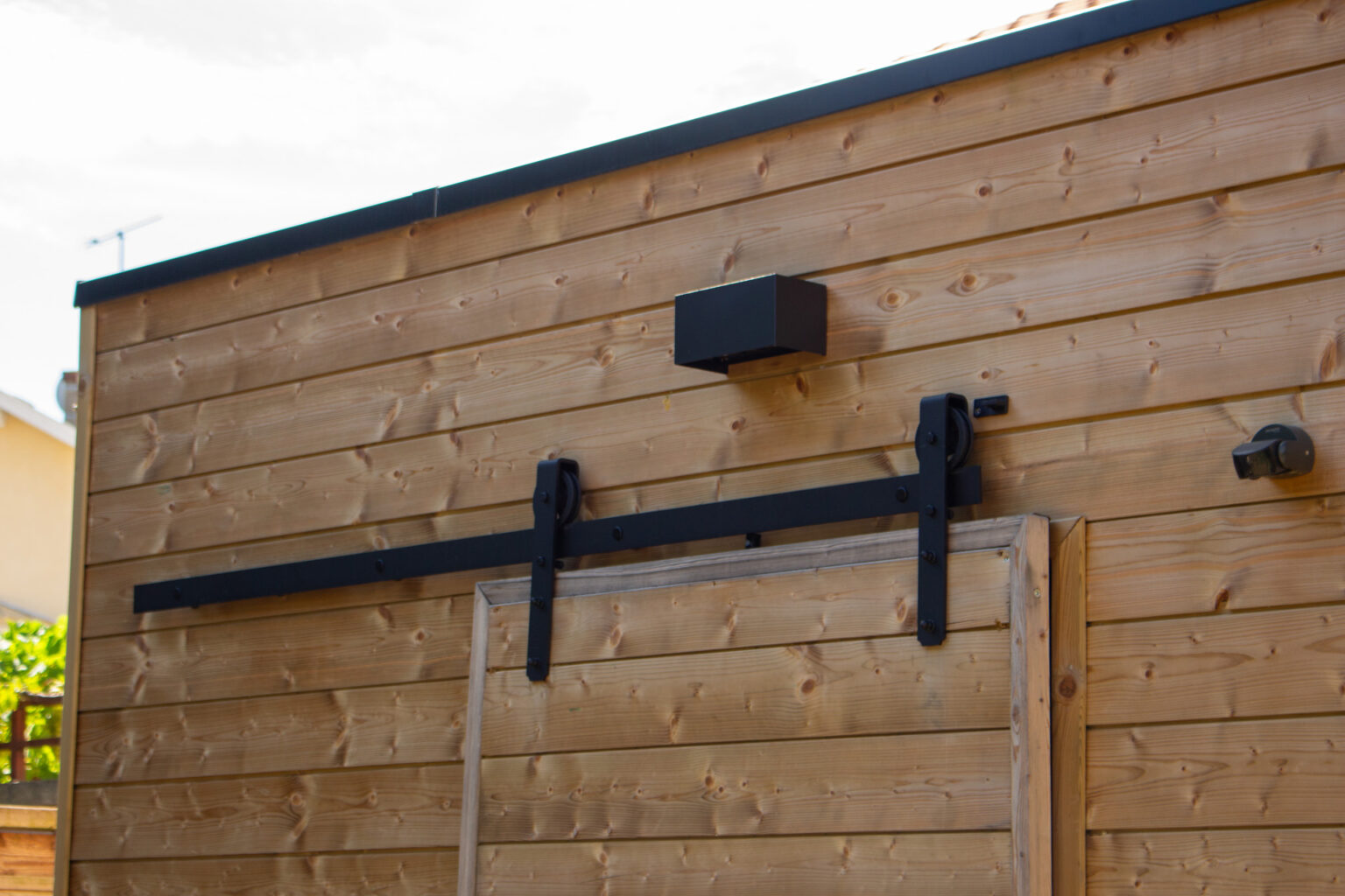 Bardage bois de l'abri de jardin à toit plat avec rail de porte coulissante noir et applique – projet BETULA