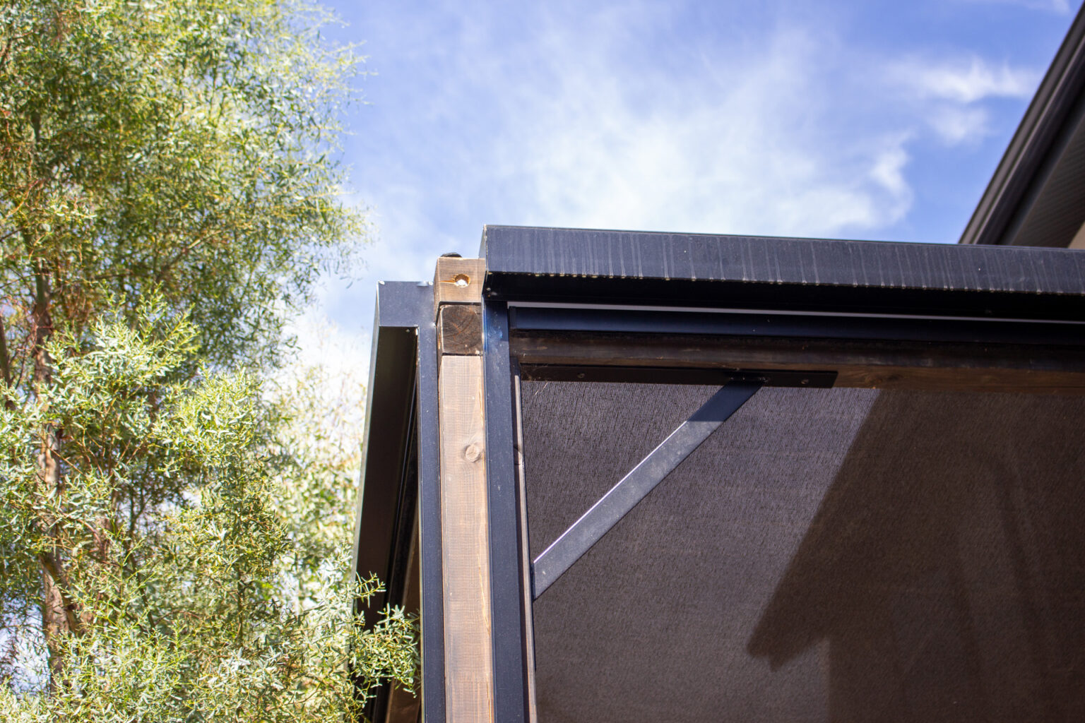 Angle de la pergola bois noire avec coffre de store zip et toile micro-perforée, en contre-plongée – projet BETULA