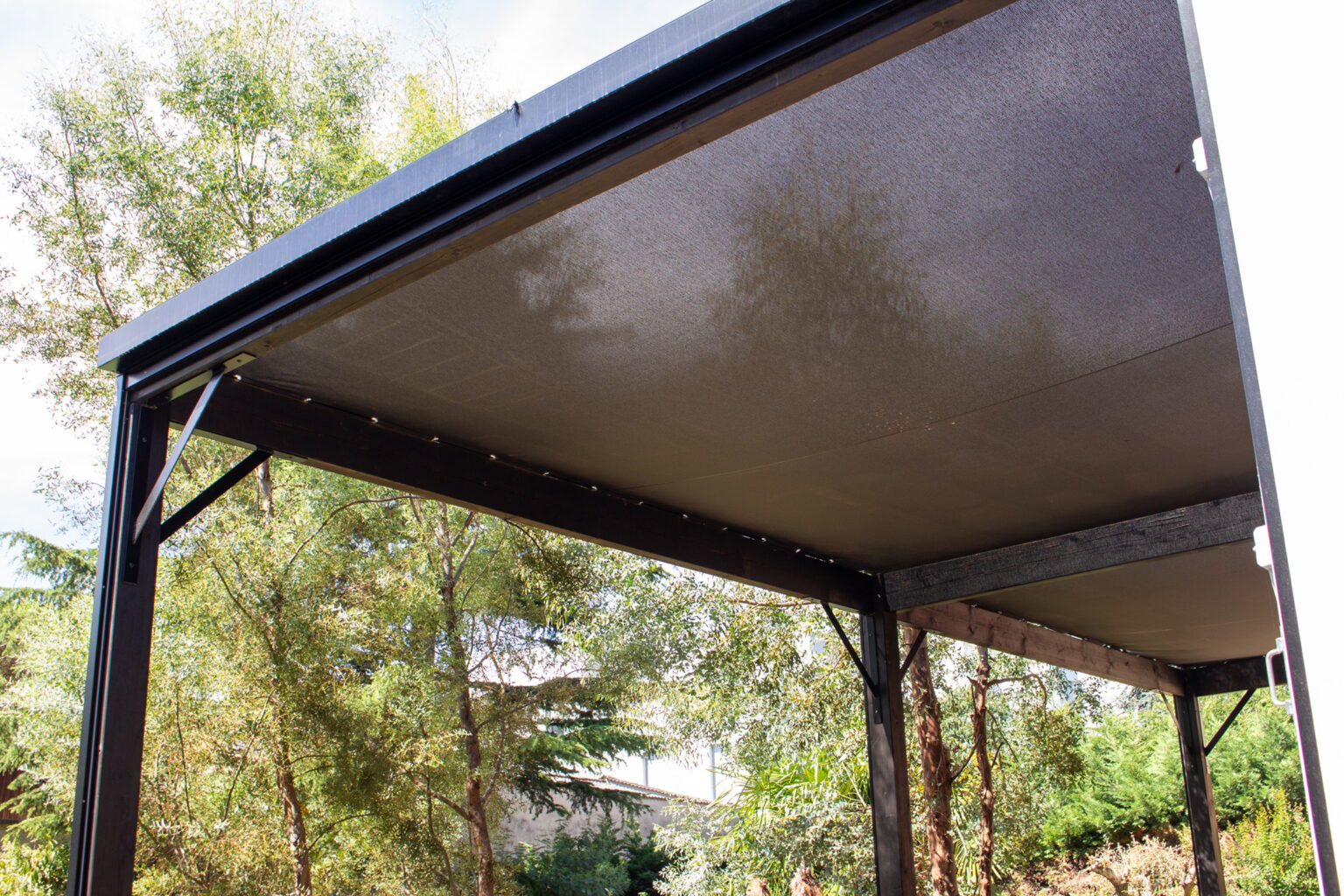 Sous-face de la pergola bois avec toile micro-perforée tendue et poteaux noirs à équerres – projet BETULA