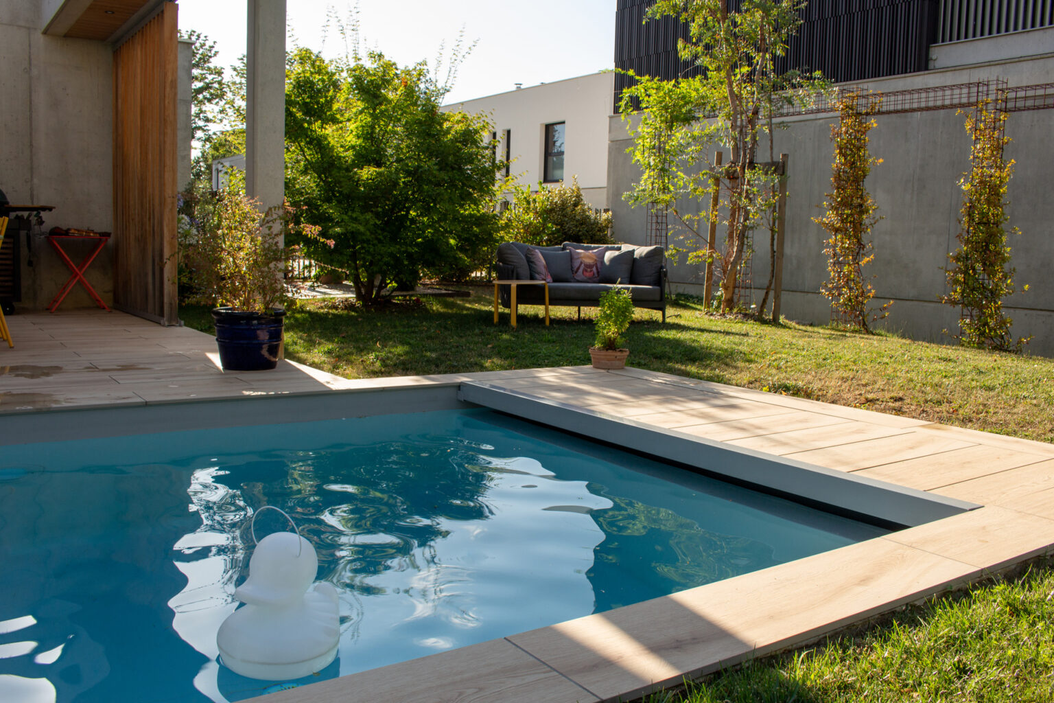 Plage de piscine en dalles claires, pelouse, salon d'extérieur et colonnes acier végétalisées – projet BUXUS