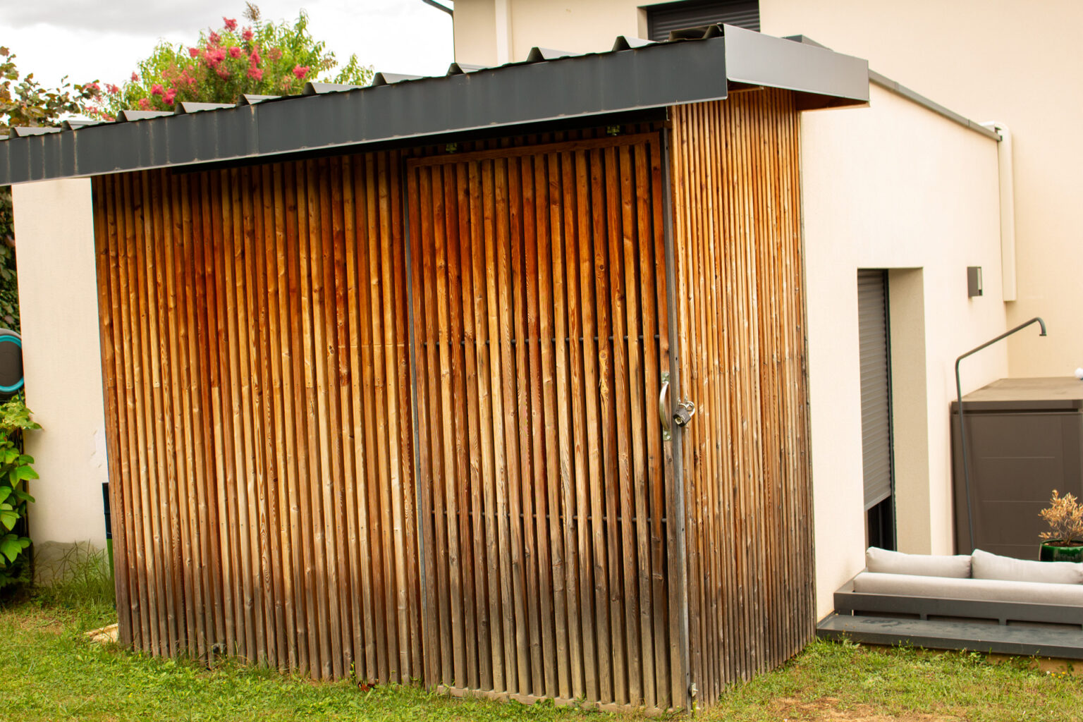 Abri de jardin en bardage bois vertical avec porte coulissante intégrée, canapé d'extérieur à côté – projet BAOBAB