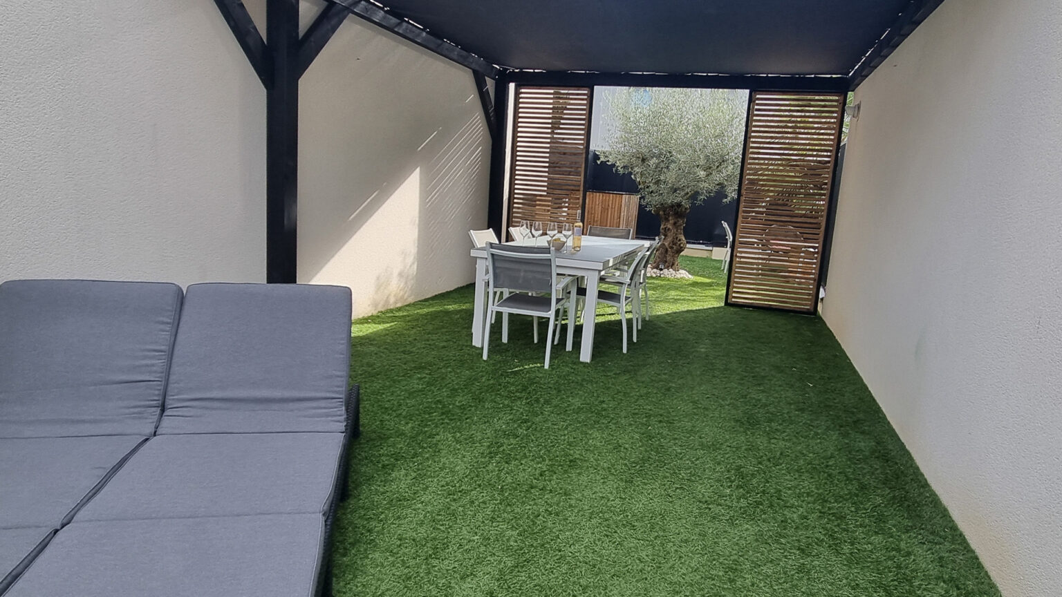 Espace repas sous la pergola bois teinté noir, gazon synthétique et panneaux coulissants en mélèze – projet GAURA