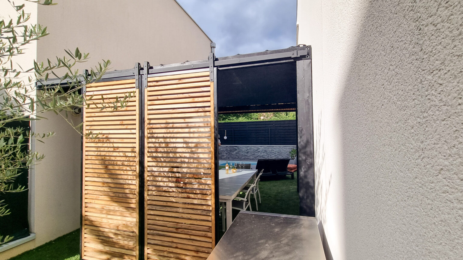 Deux panneaux coulissants en claire-voie mélèze refermés devant la pergola, ouverts sur la piscine – projet GAURA