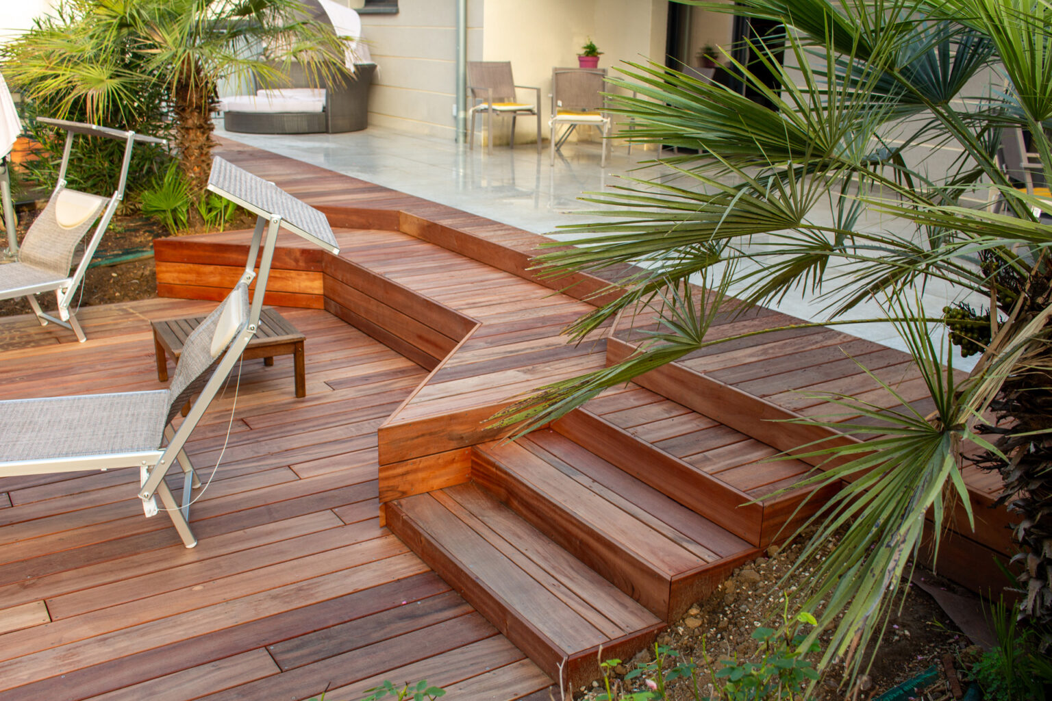 Plage bois, banquettes et escalier vus à travers un palmier chamaerops, terrasse en grès cérame au fond – projet LAVANDULA