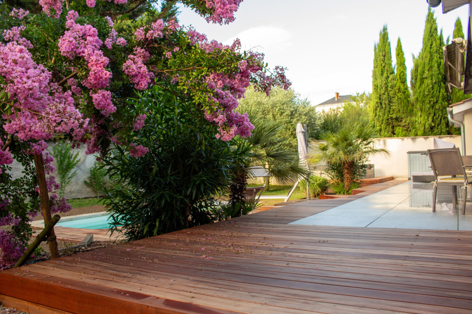 Cheminement en bois exotique vers la piscine sous un lagerstroemia rose, cyprès et palmiers au fond – projet LAVANDULA