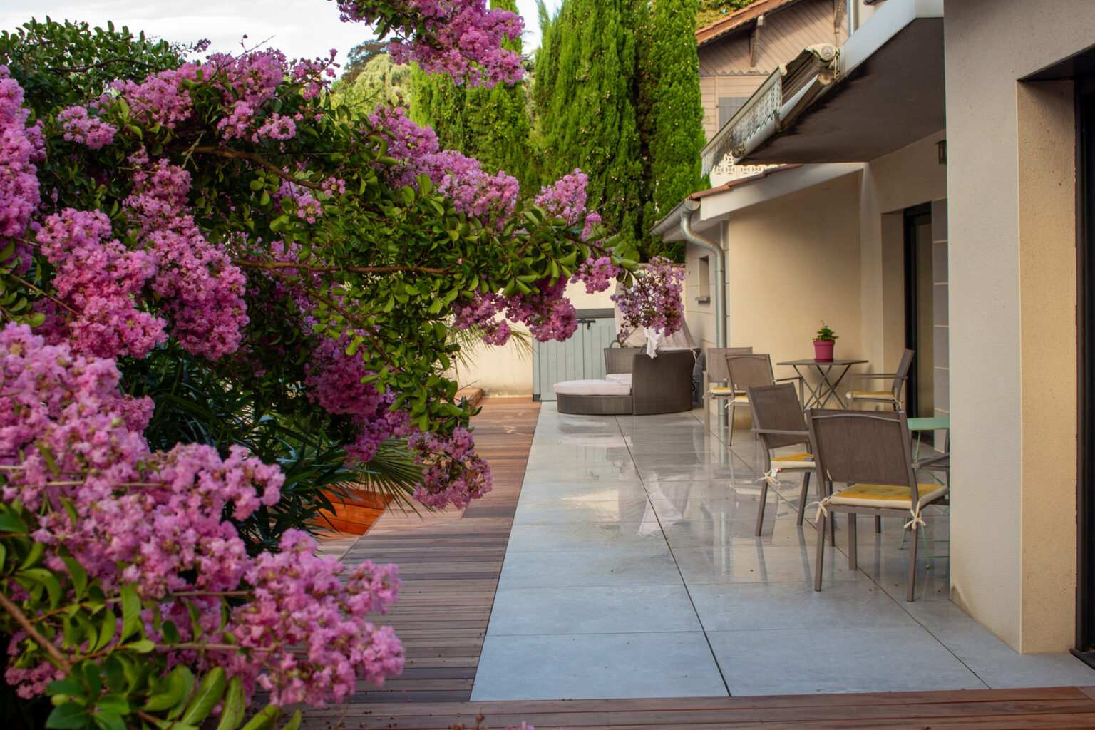 Terrasse en grès cérame bordée d'une bande en bois exotique, salon de jardin et lagerstroemia rose – projet LAVANDULA