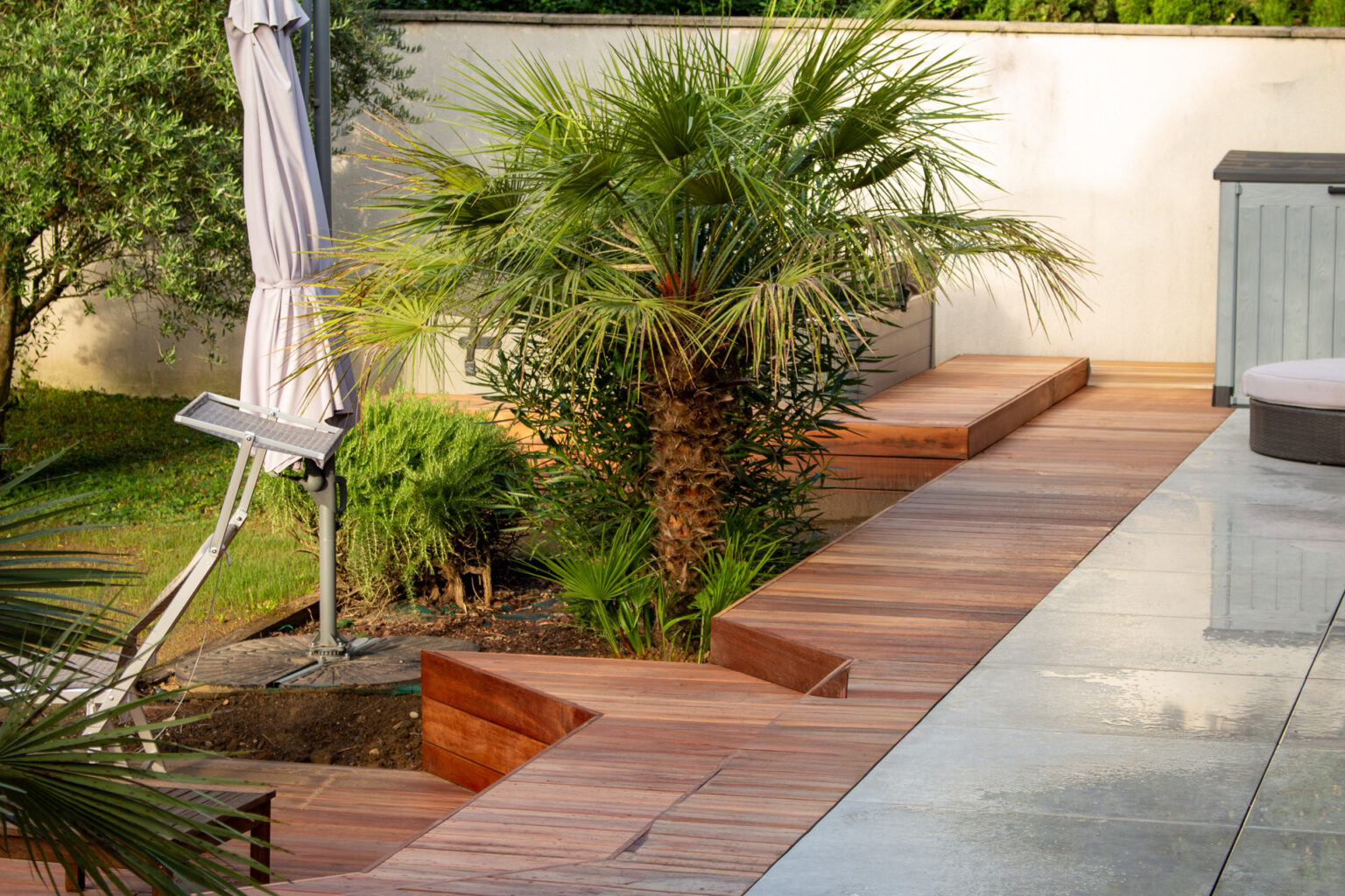 Banquettes en bois exotique le long du mur enduit, palmier chamaerops, parasol et terrasse grès cérame – projet LAVANDULA