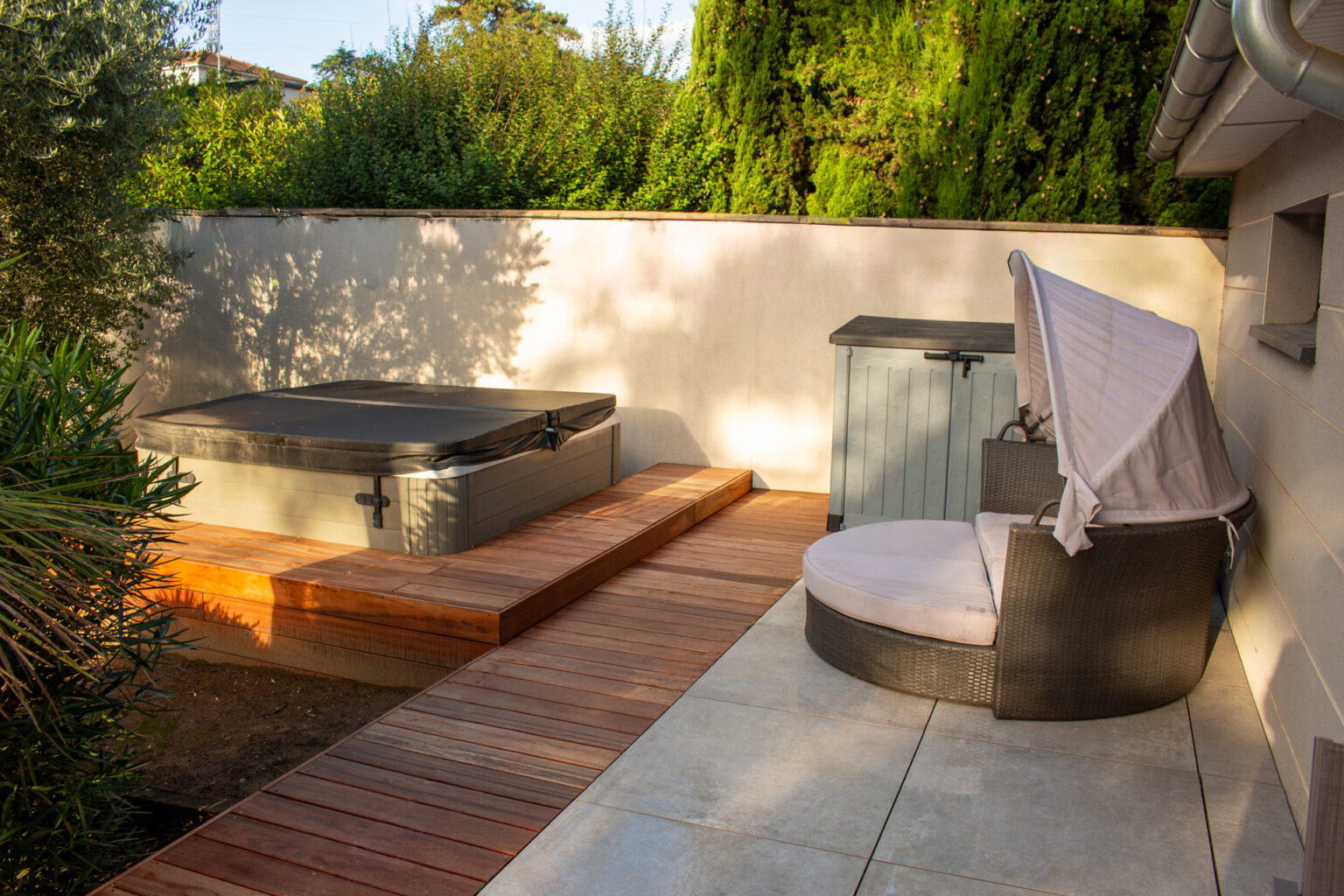 Spa couvert sur estrade en caillebotis bois, coffre et lit de jour tressé sur terrasse en grès cérame – projet LAVANDULA