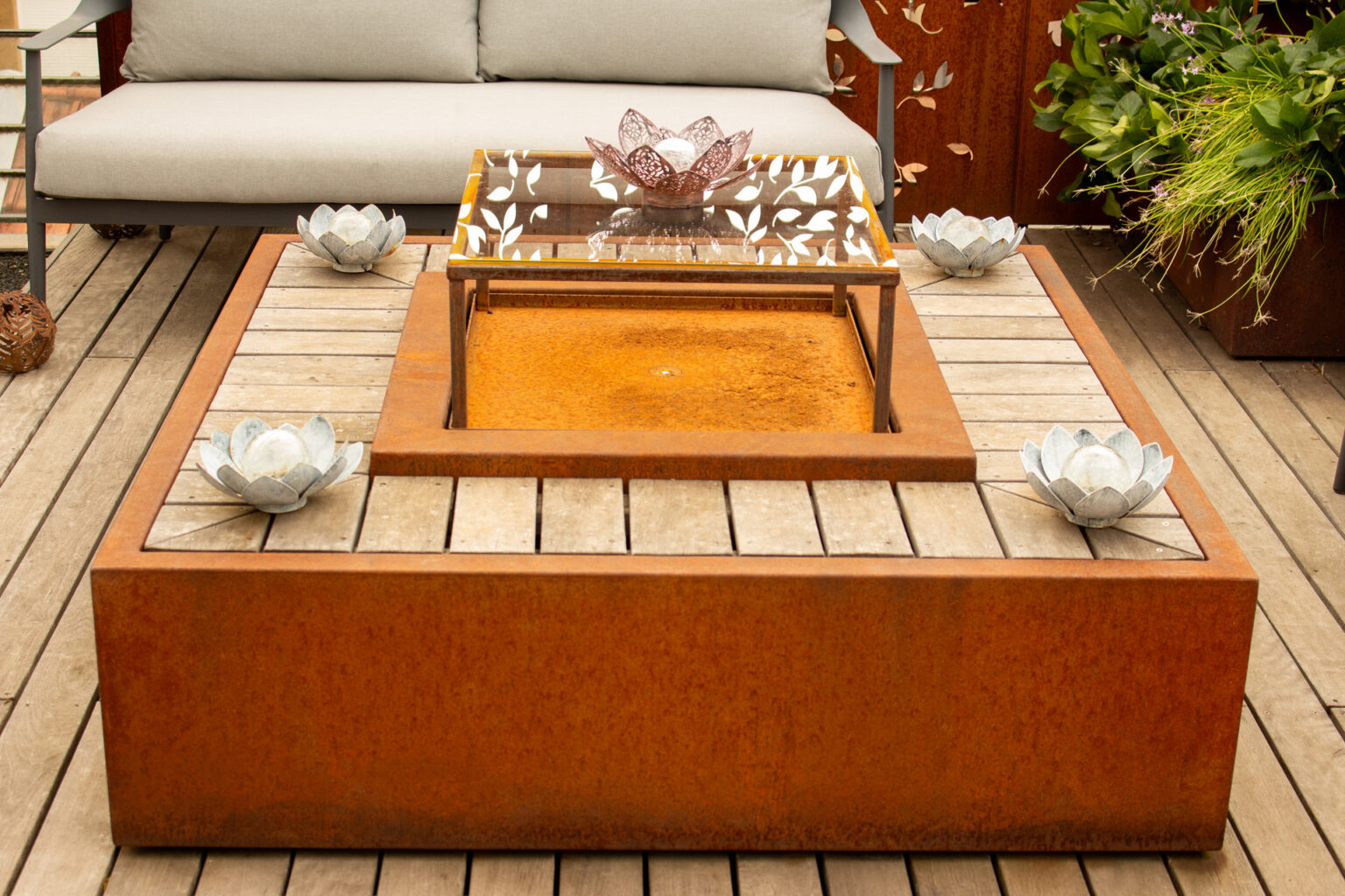 Gros plan sur la table d'eau en corten et ipé, plateau en verre trempé sur support acier, nénuphars métal – projet PAEONIA