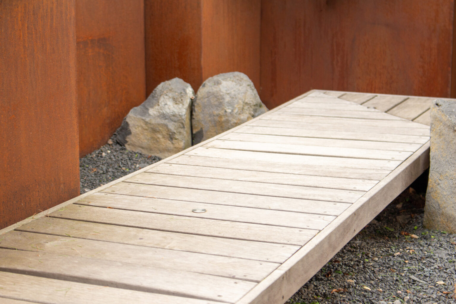 Gros plan sur un ponton en lames d'ipé posé sur gravier, rochers et parois de bacs en corten – projet PAEONIA