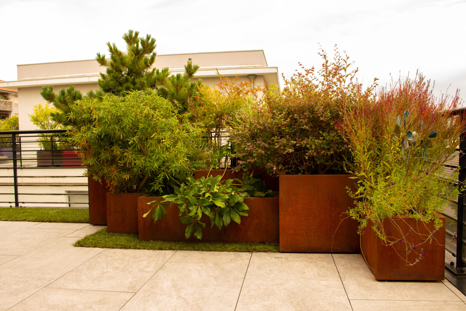 Enfilade de bacs en corten de hauteurs différentes, gazon synthétique et dalles de grès cérame – projet PAEONIA