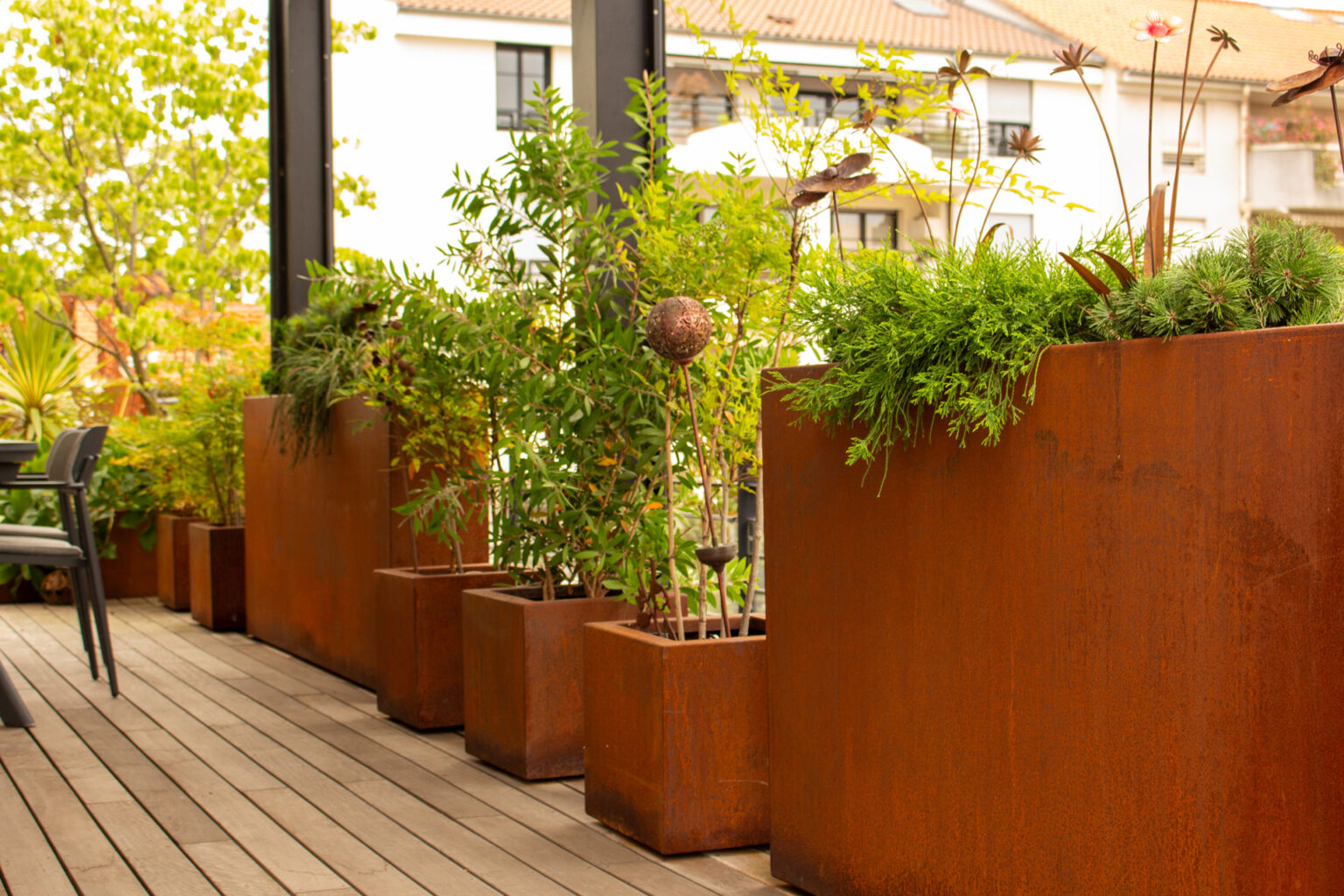Bacs en corten alignés sur un ponton en ipé, plantés d'arbustes et de vivaces, sculptures métalliques – projet PAEONIA