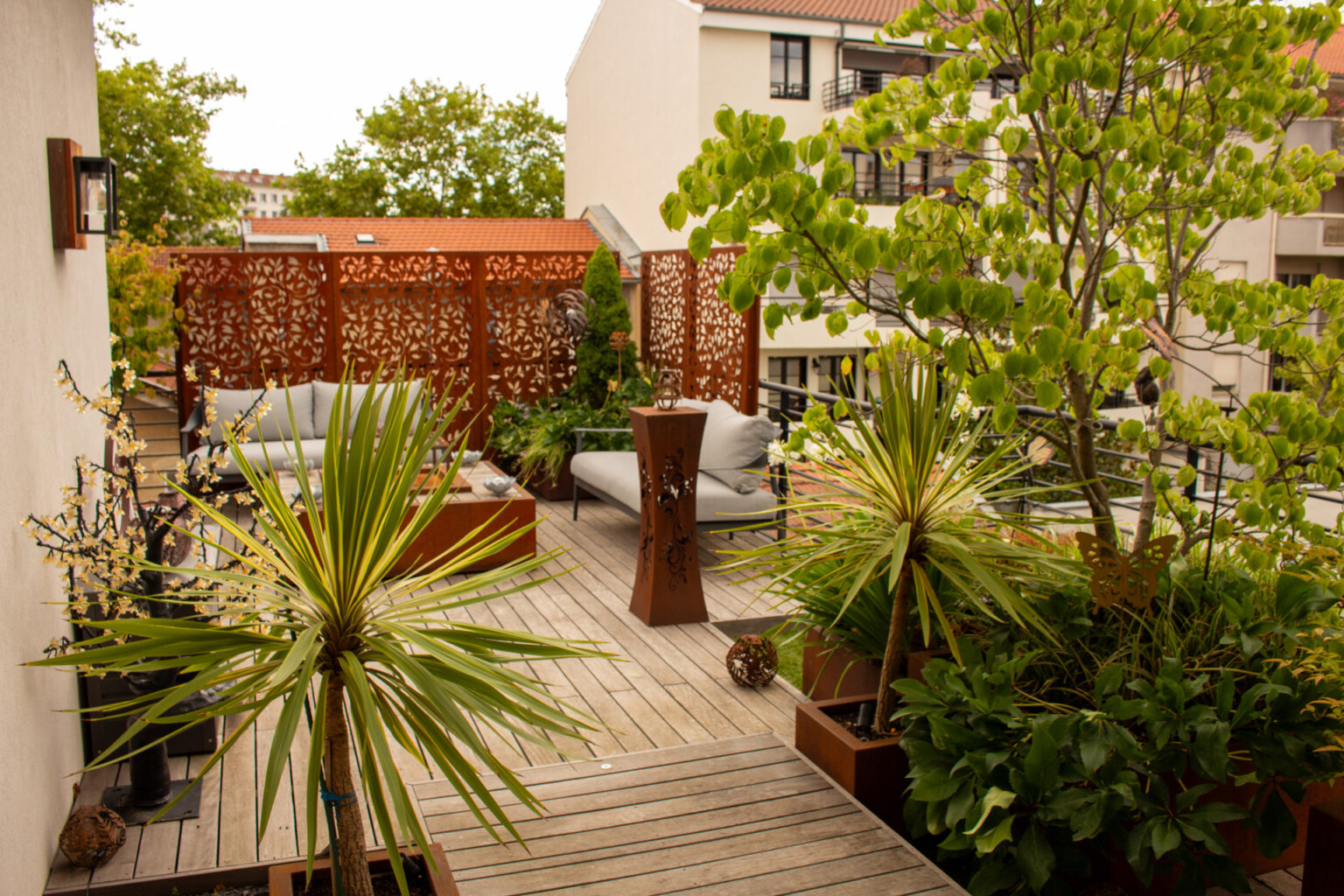 Espace cosy sur ponton en ipé avec canapés, claustras en corten ajouré, lanterne et cordylines – projet PAEONIA