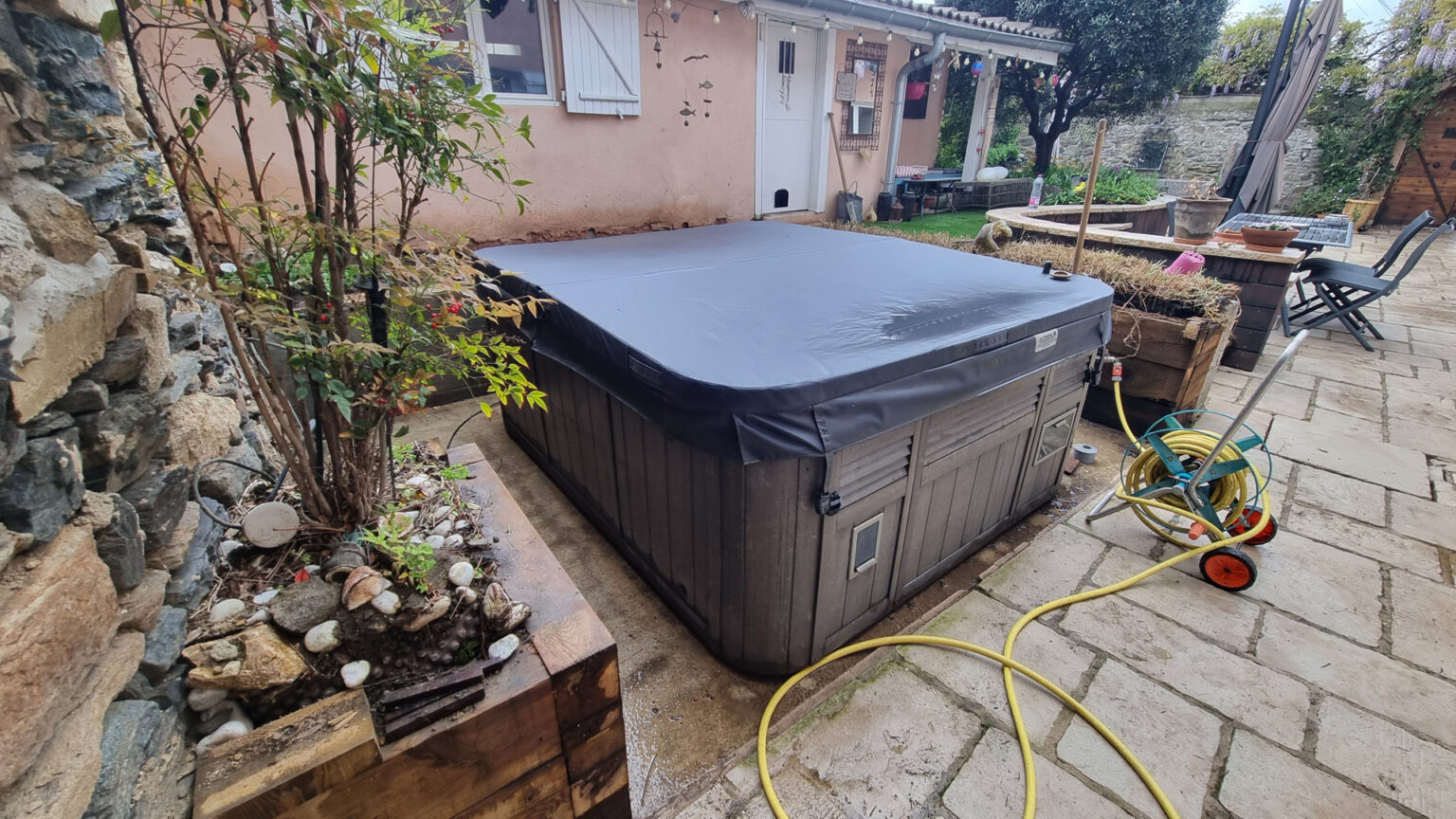 Avant travaux : spa couvert sans habillage dans une cour dallée de maison de village, vieille jardinière – projet SYRINGA