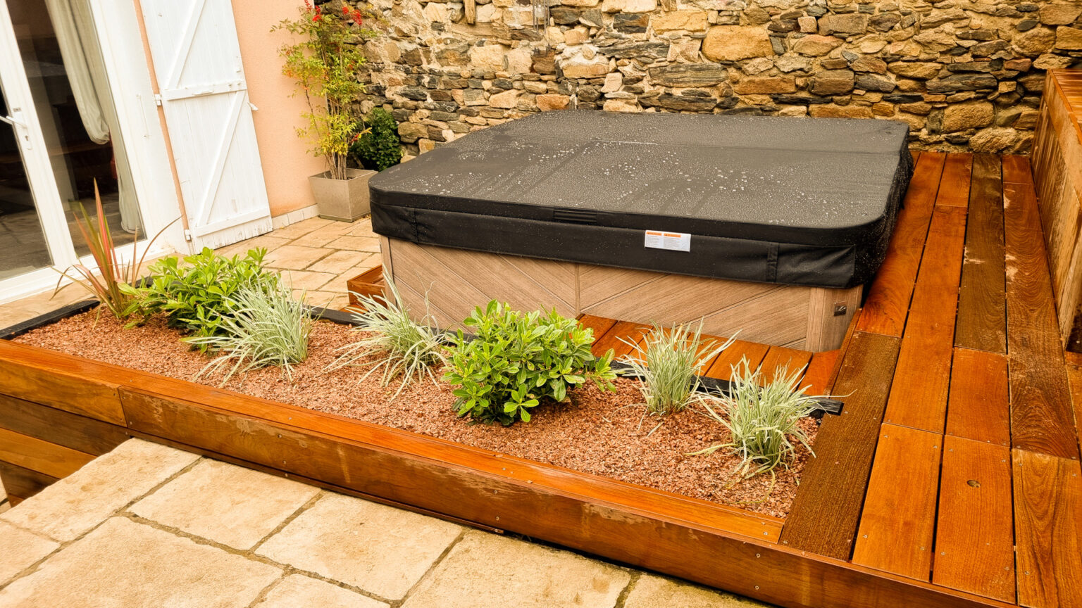 Spa couvert entouré de sa plage ipé et d'une jardinière bois plantée d'arbustes bas, façade à gauche – projet SYRINGA