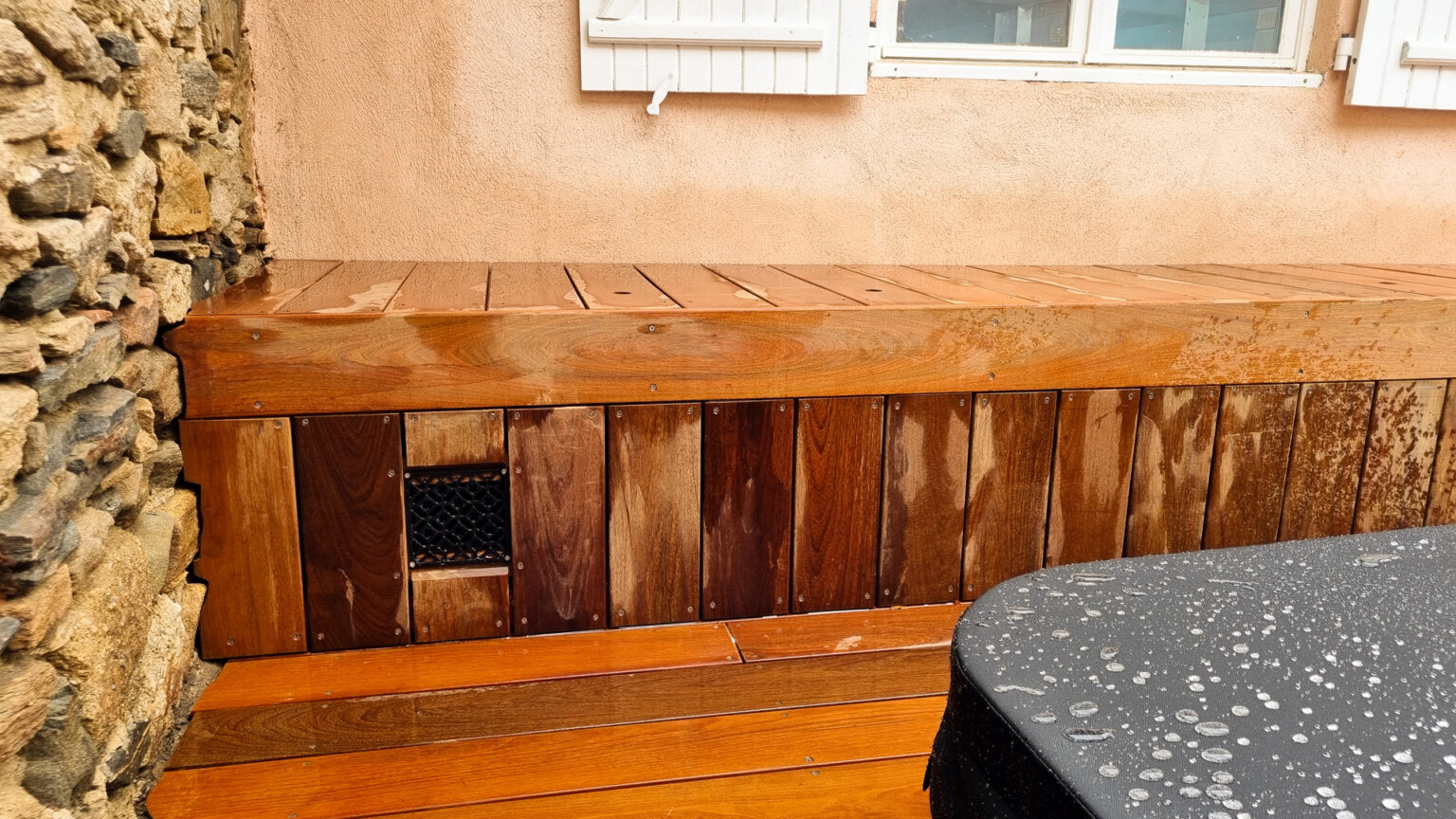 Détail de la banquette-coffre en lames verticales de bois exotique avec grille d'aération, capot du spa – projet SYRINGA