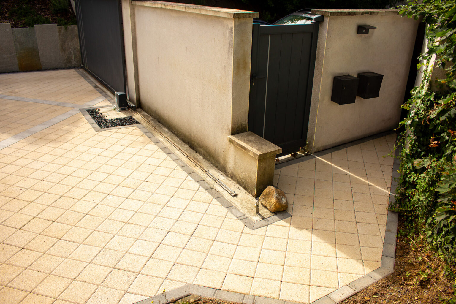 Pavage drainant beige à bordures grises devant un portillon et des boîtes aux lettres, caniveau en concassé – projet ULMUS