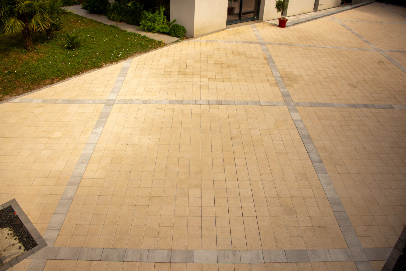Pavés drainants beiges quadrillés de bandes grises dessinant la ligne de fuite vers la porte d'entrée – projet ULMUS
