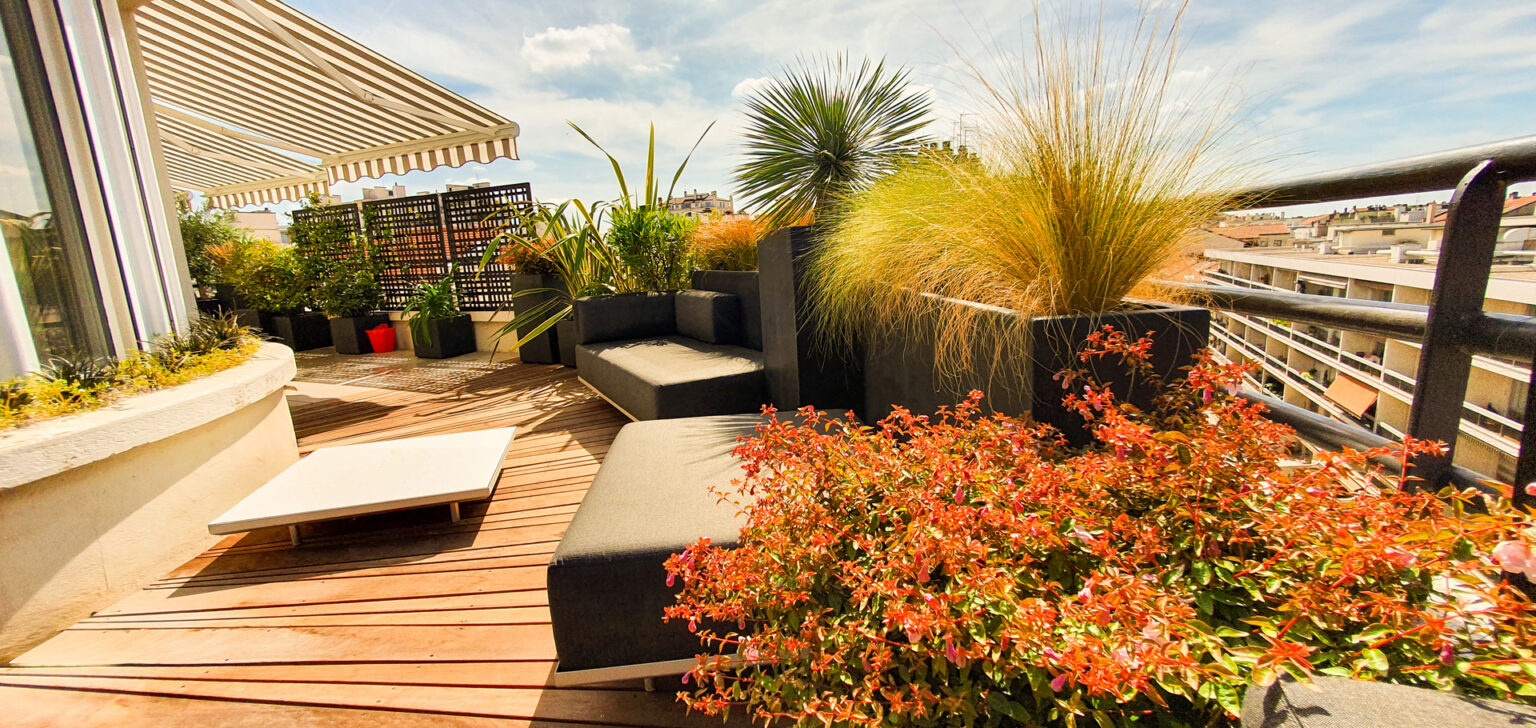 Abélia fleuri et stipa dorées en bacs anthracite près du salon lounge, store banne rayé au-dessus – projet SEDUM