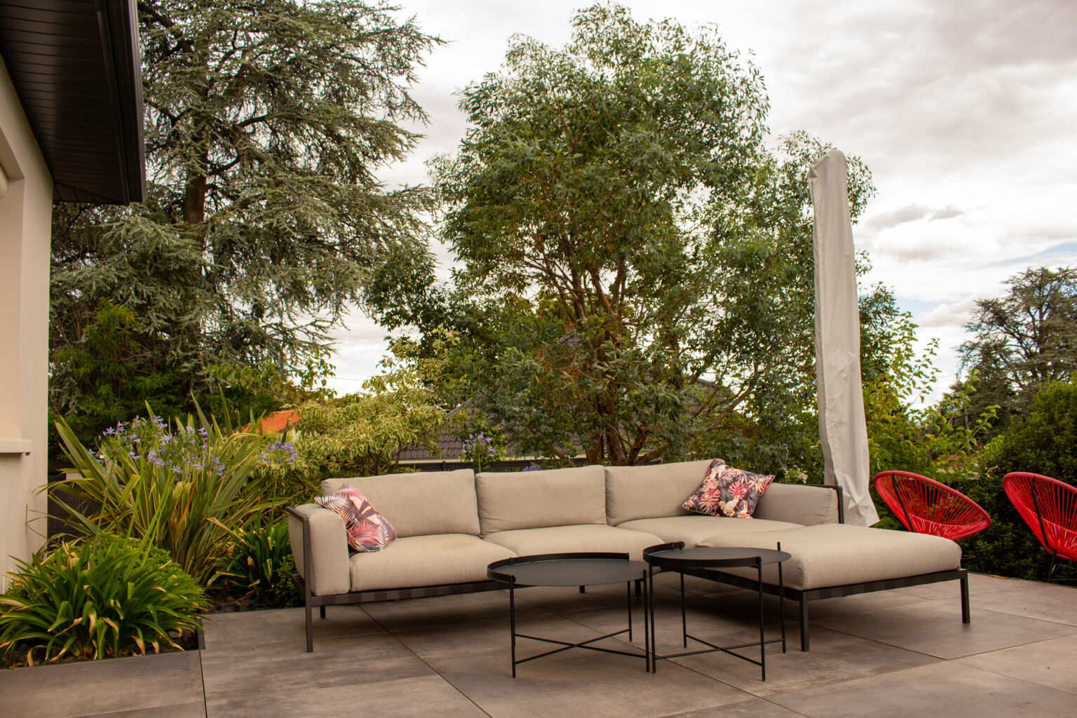 Salon de jardin sur la grande terrasse dallée, agapanthes et phormiums en bordure, fauteuils rouges – projet SALVIA