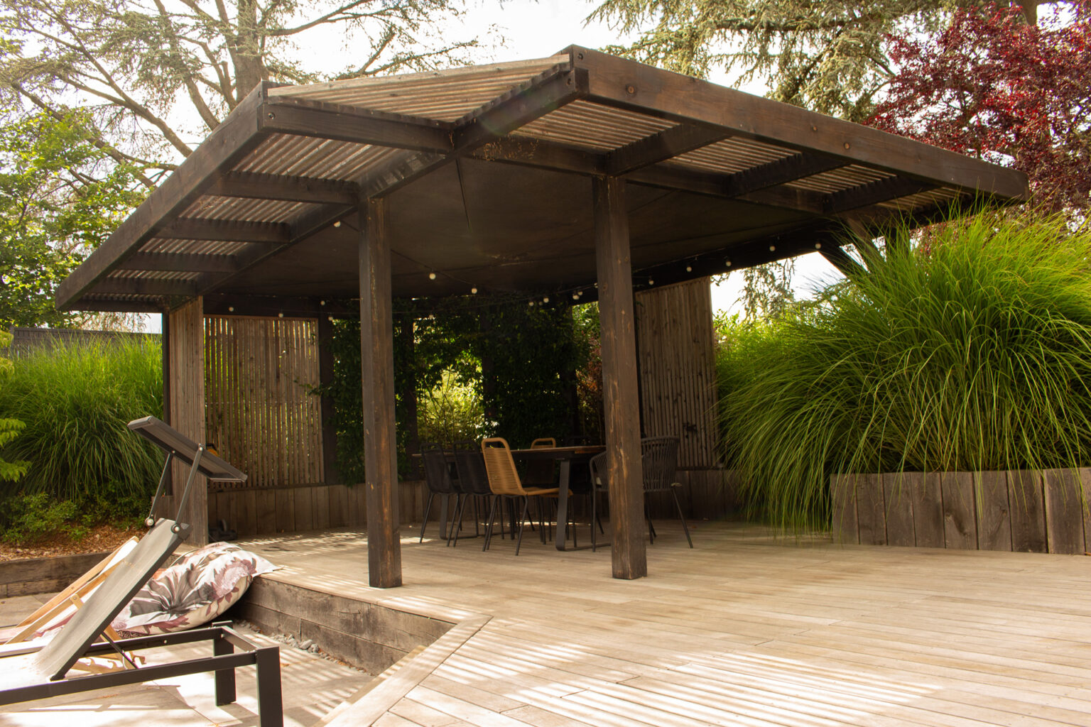 Pergola bois sur mesure à casquette déportée sur deux faces et brise-vue en tasseaux, table sur platelage – projet SALVIA