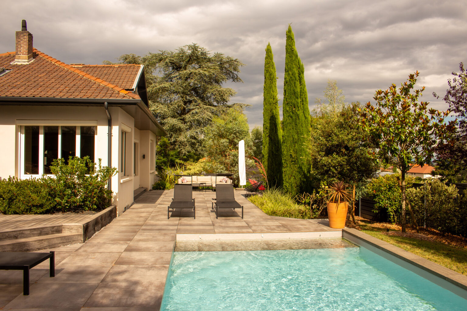 Piscine et grande terrasse dallée devant la maison, bains de soleil, cyprès et cèdre bleu en arrière-plan – projet SALVIA