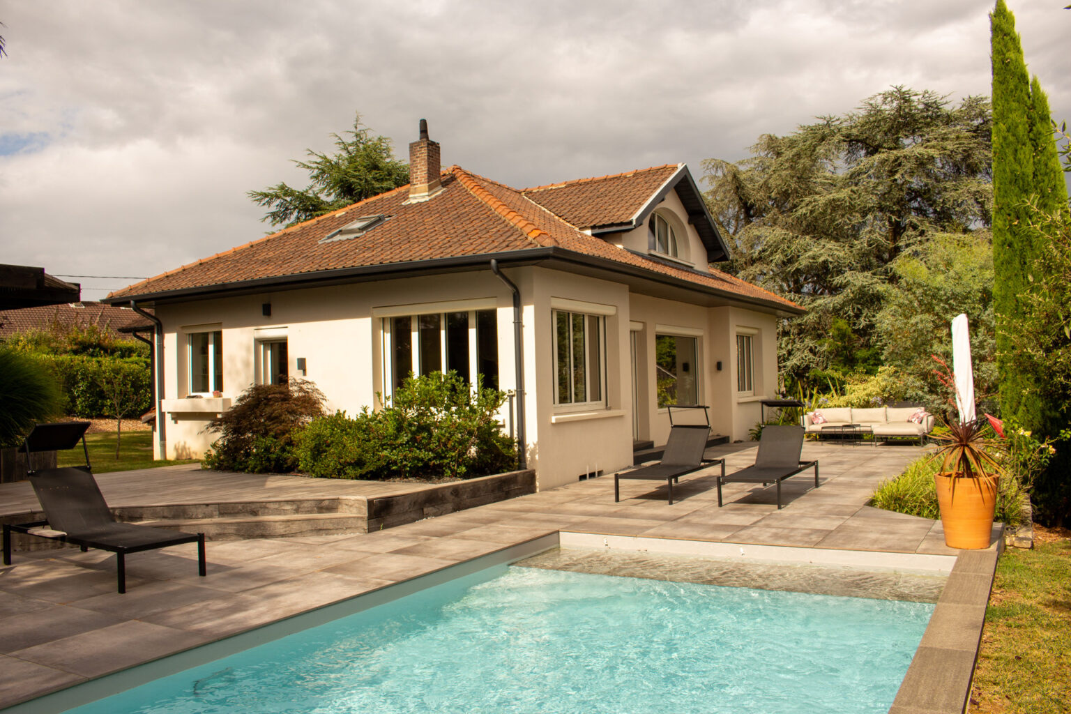 Piscine avec plage immergée et terrasse dallée face à la maison, bains de soleil, cordyline en pot orange – projet SALVIA