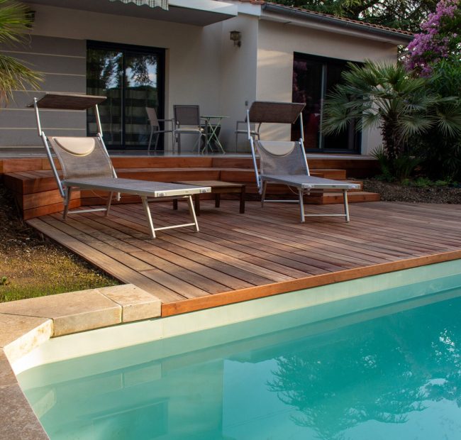 Bains de soleil sur la plage bois au bord de la piscine, maison et lagerstroemia rose en arrière-plan – projet LAVANDULA